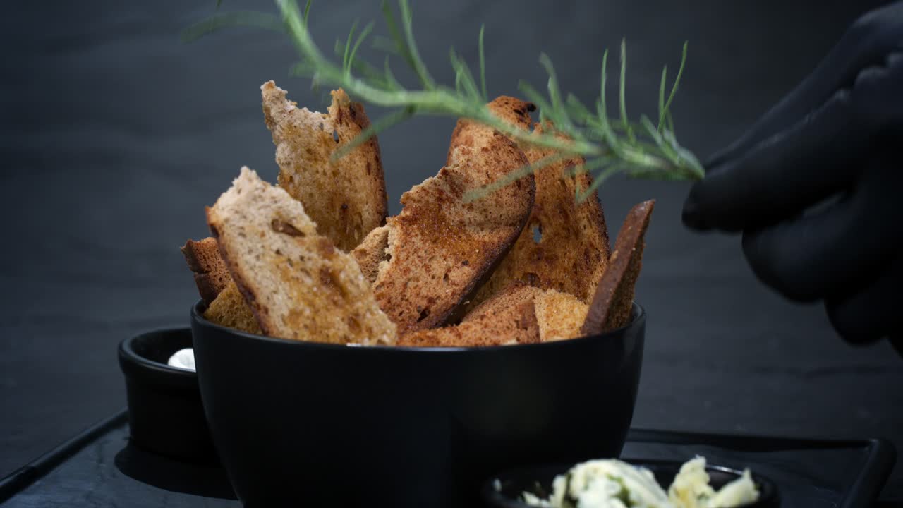 A bowl of toasted bread and herb butter is garnished with rosemary