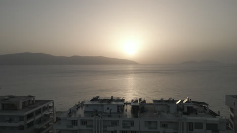 Drohnenaufnahme-über-Der-Stadt-Vlore,-Albanien,-Mit-Blick-Auf-Die-Gebäude-Und-Den-Hafen-Mit-Der-Fähre-Mit-Dem-Meer-Und-Dem-Strand-Darunter-Während-Des-Sonnenuntergangs-Am-Abend-Mit-Einem-Orange-Leuchtenden-Baumstamm