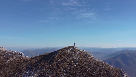 person stands on the peak of a rocky mountain drone shot