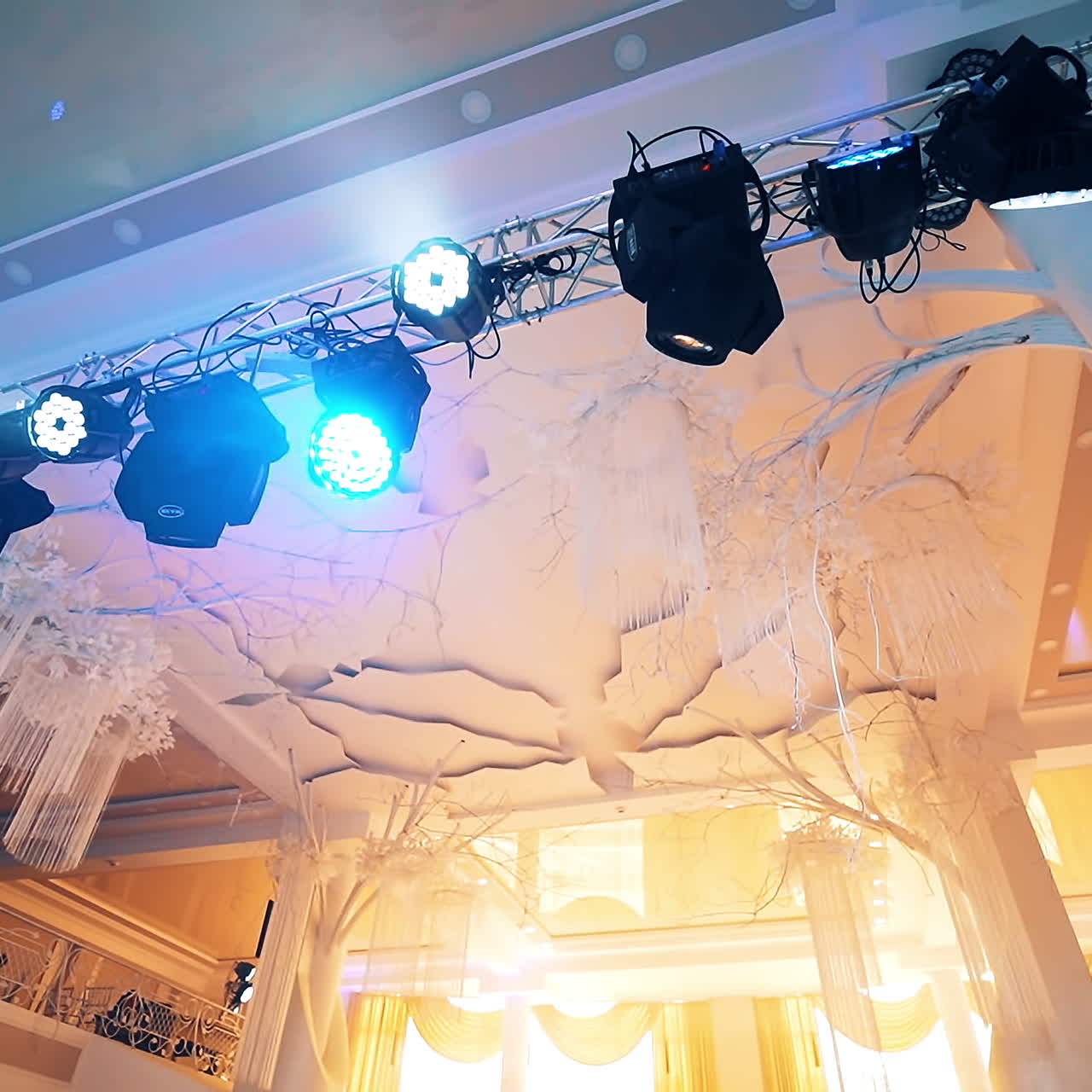 Big beautiful creamy hall and small black projectors shining from the top indoors. Metal construction with many different spotlights on the luxurious background.