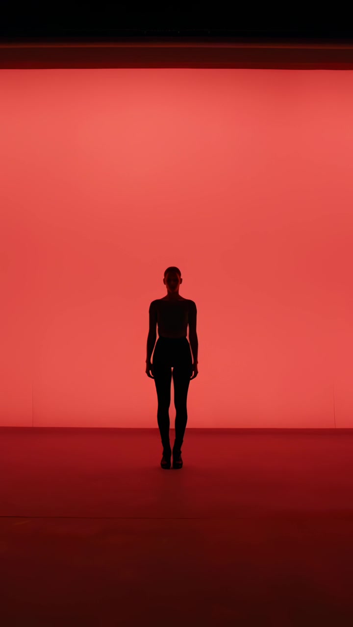 Video verticale: Donna in piedi in body che posa e si muove con un elemento che si alza su un pannello rosso dello studio.