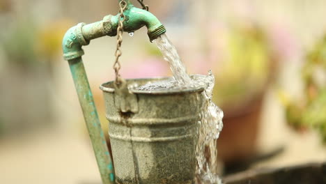 water falls in slowmotion in a garden from a diy outdoor faucet overflowing a rustic bucket into a barrel