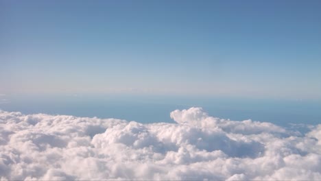 motion shot from the window of an airplane with fluffy clouds beneath and a blue sky above