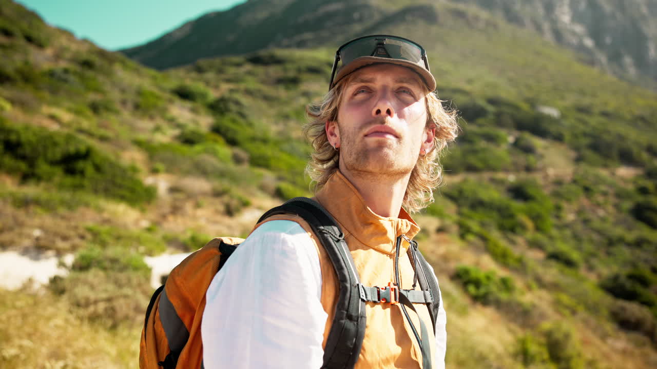 Young Man with Backpack Looking Around on a Sunny Mountain Trail