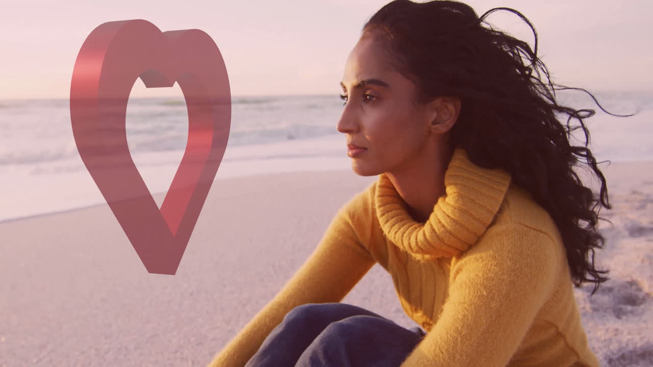 Woman in yellow sweater sitting on beach with heart shape animation over ocean