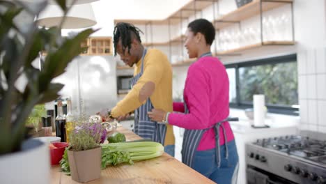 Glückliches-Afroamerikanisches-Paar-In-Schürzen,-Das-Essen-In-Der-Küche-Zubereitet,-Zeitlupe