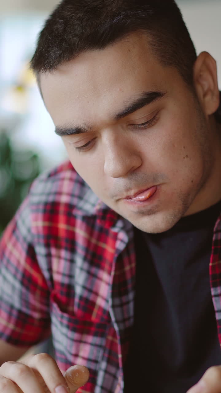 a man in a plaid shirt is eating delicious pizza at a pizzeria in the afternoon. Vertical video