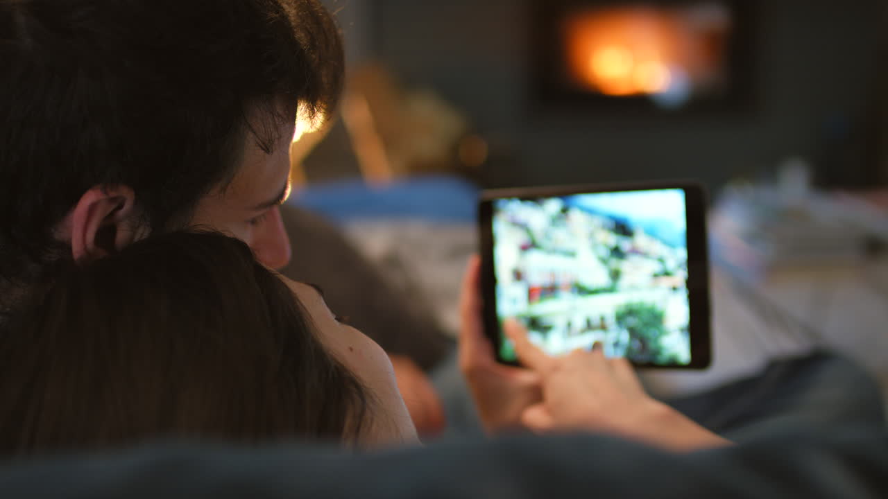 pareja relajándose junto a la chimenea, mirando fotos en una tableta
