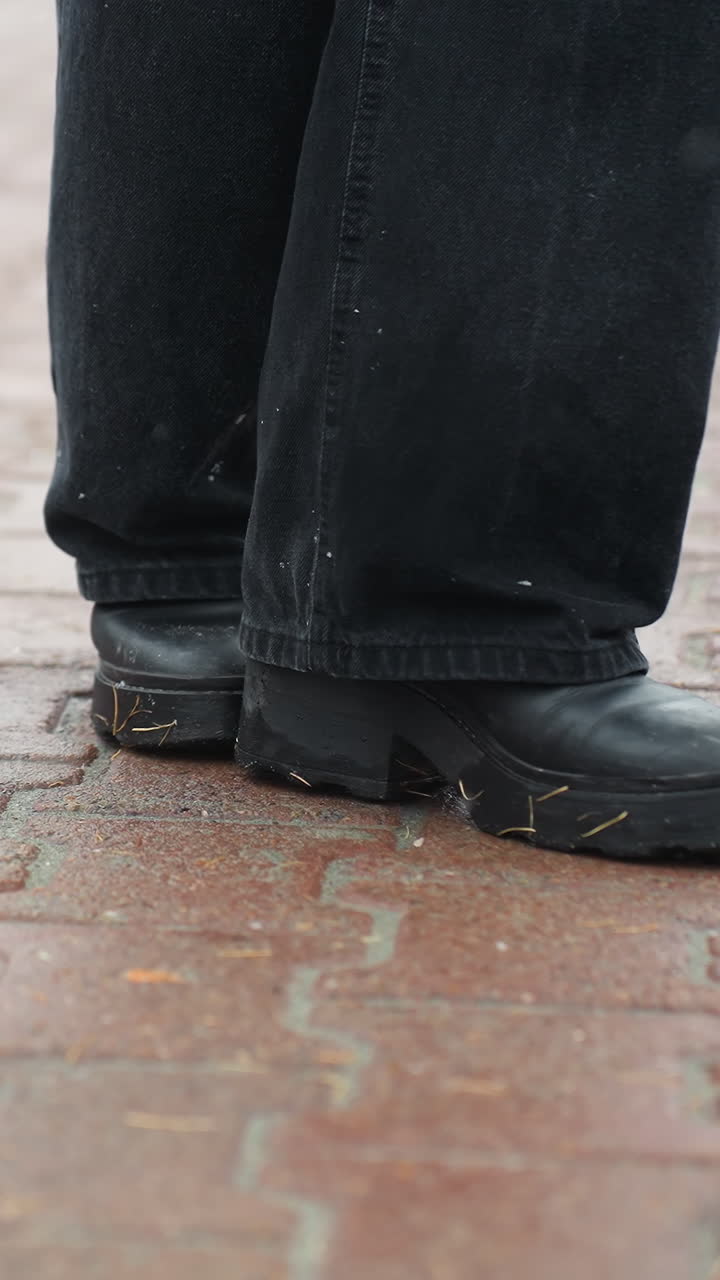 Foot of person wearing black trousers and black boots turning on wet ground, creating ripples on surface, highlighting motion in urban setting after rain, walking on pavement or outdoor surface