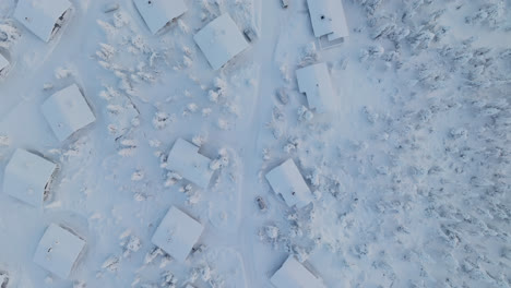 top down drone shot over snowy cabins on top of a fell, polar night in lapland