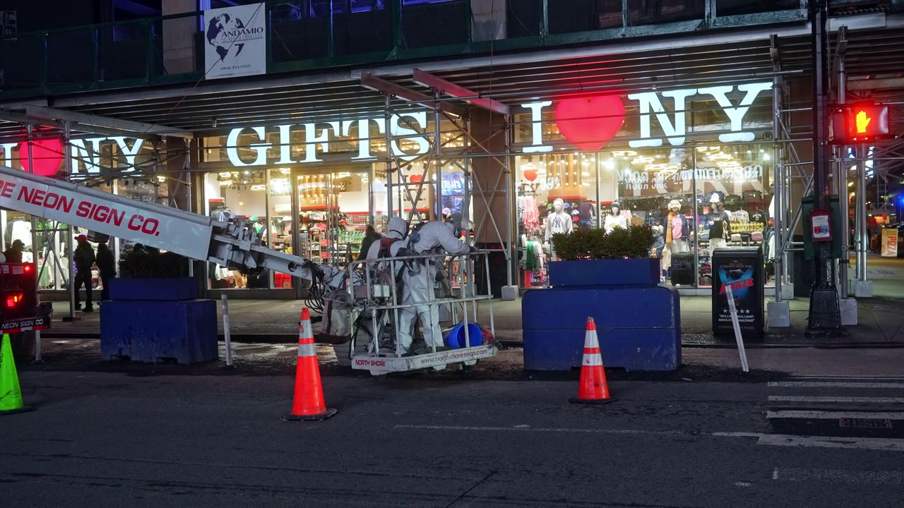New York, USA, 18 March 2026: Technicians in white suits on lift platform at night. Two workers wearing white protective gear work from cherry picker bucket near Manhattan gift shop at night.