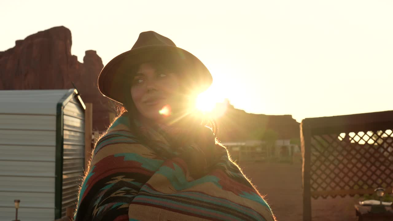 Donna sorridente con cappello e coperta contro il tramonto nel deserto