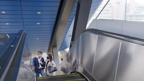 hombre de negocios y mujer de negocios montando escaleras mecánicas en la estación de tren usando máscaras faciales de ppe en la pandemia