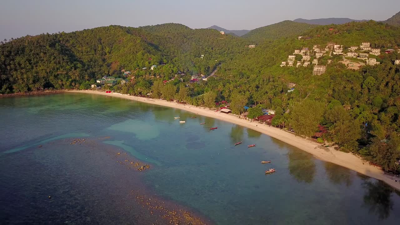 un dron aéreo de 4k empuja la toma de la playa de ensalada en koh phangan en tailandia con barcos de pesca, agua verde azulado, coral y selvas verdes