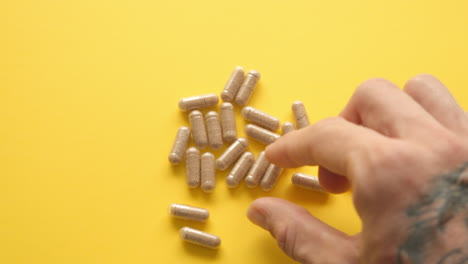 male hand picking up lions mane supplement pill from yellow table