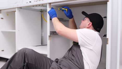a qualified craftsman in special clothes installs furniture using an electric drill