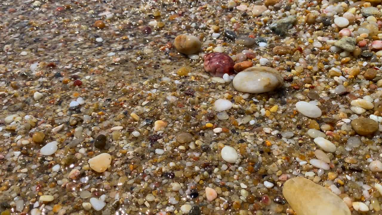 Waves hitting beautiful colourful natural stones rocks sand in sea water at the beach in Cavali&egrave;re Lavandou South of France, nature holiday vacation, 4K static shot