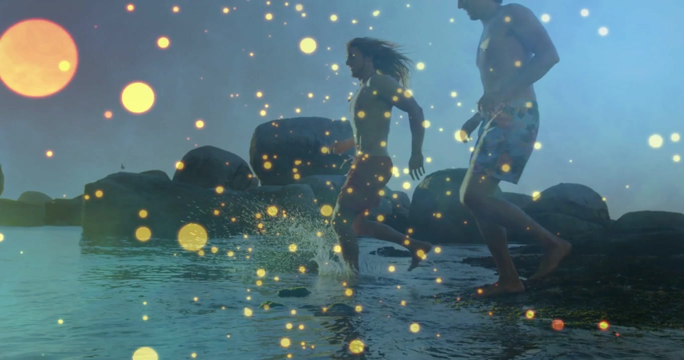 Travel woman stepping off rock into surf, man following, golden bokeh overlaying, splashes growing