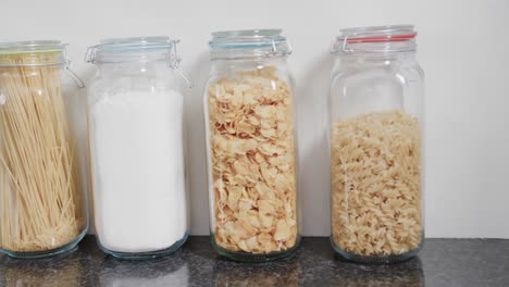 close up of food storage jars with flour and various kinds of pasta on shelf in kitchen, slow motion