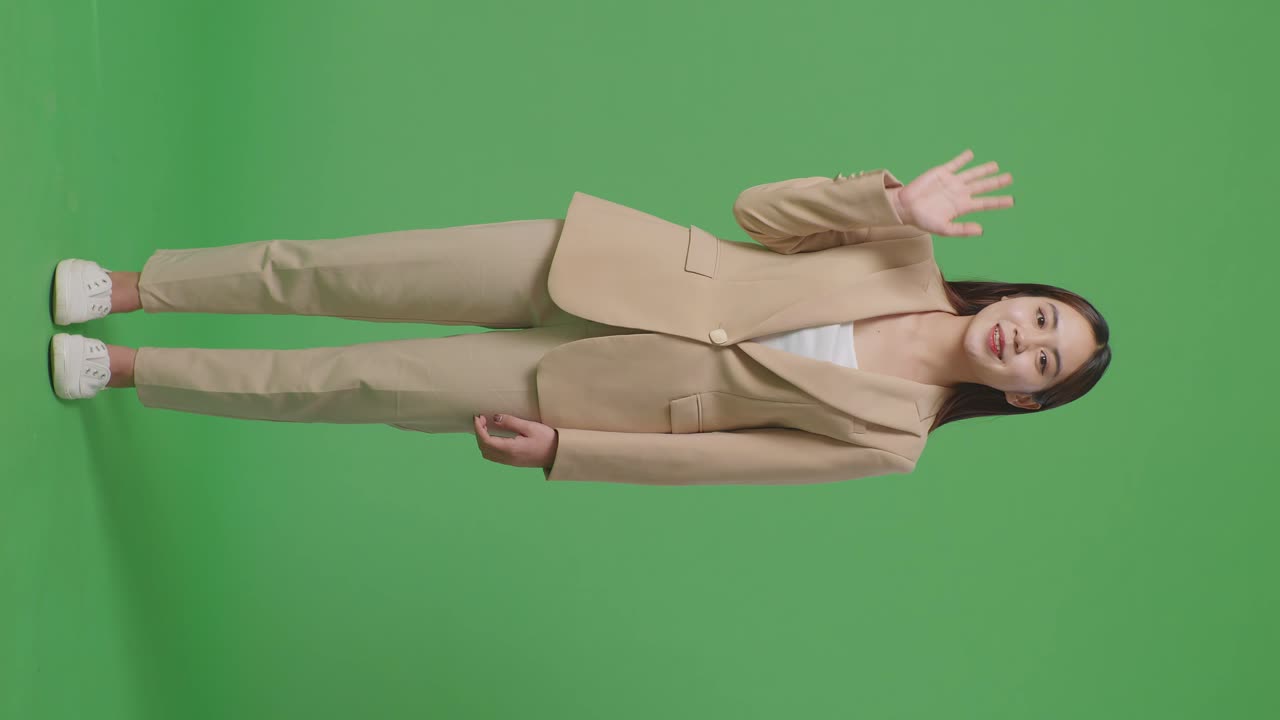 스튜디오에서 녹색 스크린에 서 있는 동안 손을 흔들고 미소 짓는 아시아 사업가의 몸이 가득 차 있습니다.