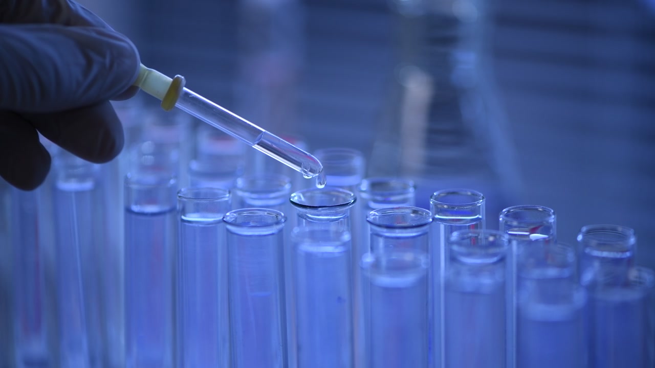 Mano guantata che rilascia liquido in provette in un laboratorio