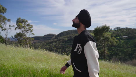 side view of an indian punjabi sikh man walking on an uphill trail along the grassy slope