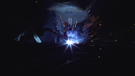 a blacksmith with a welding mask and welders leathers, is welding metal products in the garage, fire sparks fly to the sides. dark mood. slow motion shot with red monstro 8k.
