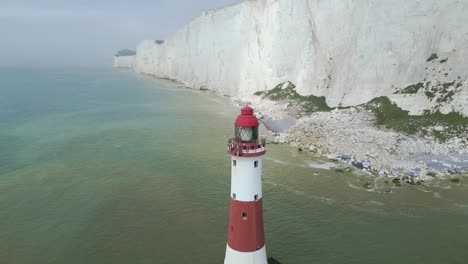 Flying-Dronie-from-Beachy-Head-Lighthouse,-white-cliffs,-foggy-sky-and-sea-taken-by-dji-mini-3-pro-drone-in-Eastbourne-England