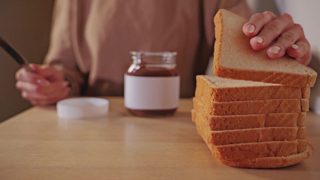 Woman picks up a knife and bread before spreading sweet chocolate paste