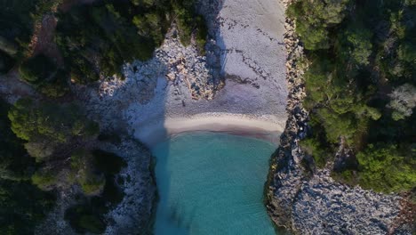 aerial view of clear blue water crashing on shore of es talaier virgin beach in menorca spain wide shot