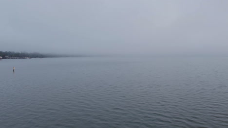 drone shot of a fogging morning on a lake with shore in the distance