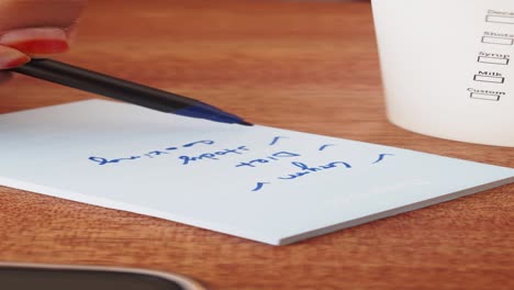 A close up of a hand writing a to-do list on a piece of paper