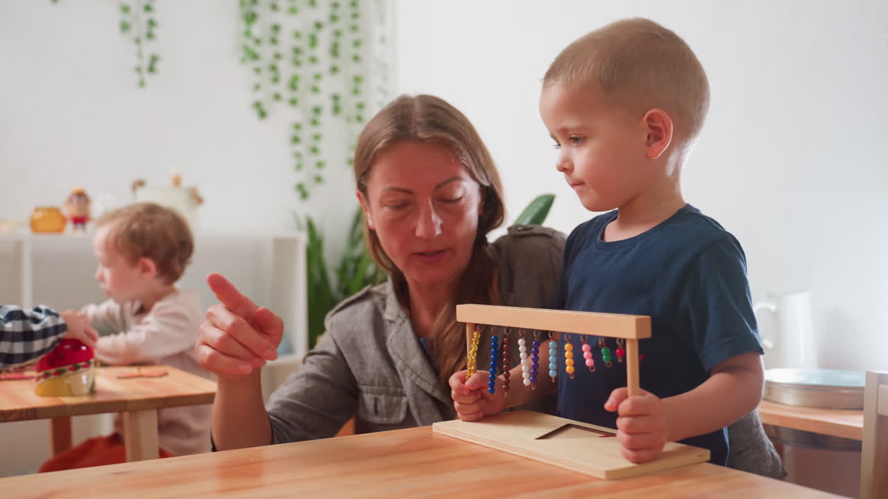 Care giver instruct child holding wooden abacus to return it, while other children remain engaged in classroom activities, capturing educational moment of early childhood learning