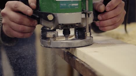 extremely close up of a craftmans hands working with polishing with manual grinding machine at wood workshop. grinds a large wooden plank. dust and chips are scattering on the floor. unrecognizable person