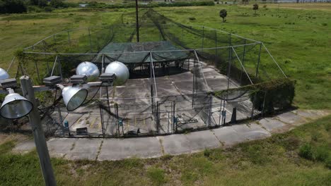 slow aerial of an abandoned amusement batting practice cage, dramatic flight by old lighting