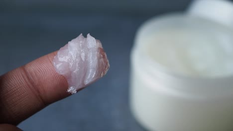 finger holding a small amount of white creamy lotion or ointment