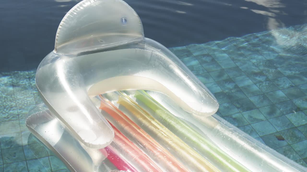 Clear pool lounger is bobbing, drifting on tiled ledge as breeze ripples move it, tubes glinting