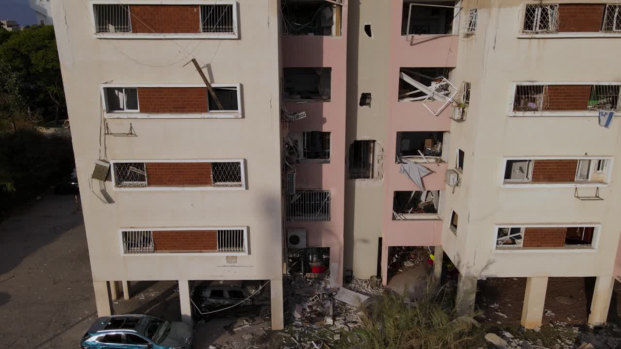 Drone descends along a Tel Aviv building damaged by an Iranian missile, showing shattered windows and debris