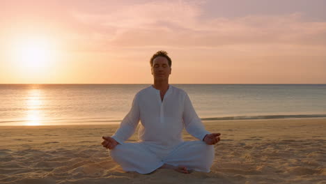 man meditating on a beach at sunset