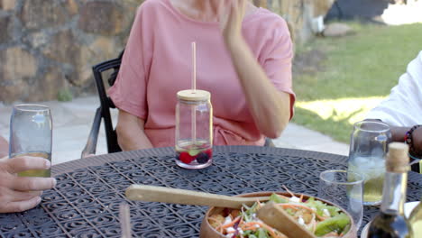 enjoying in garden lunch, diverse seniors sharing salad and drinks at garden table