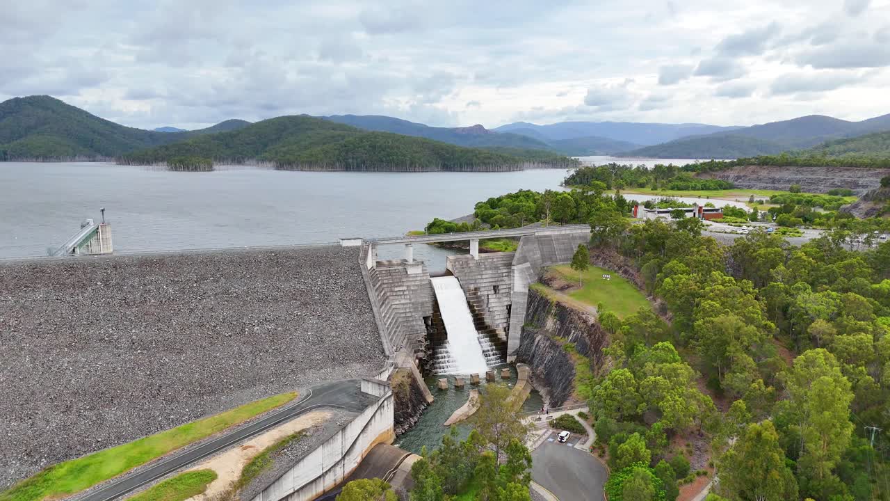 Water flows over dam surrounded by lush landscape