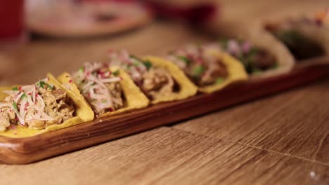 a series of tacos arranged on a wooden platter in a warmly lit restaurant setting, highlighting vibrant ingredients