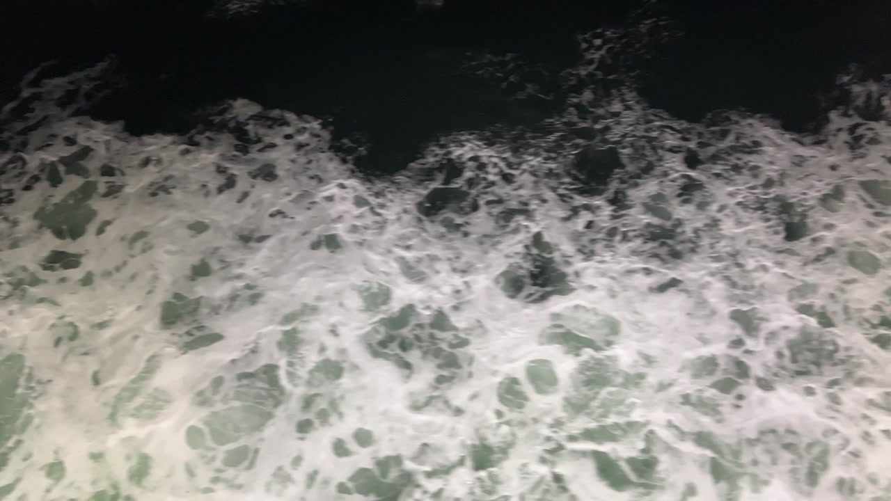 Looking down from a ship at sea wake foaming at night.