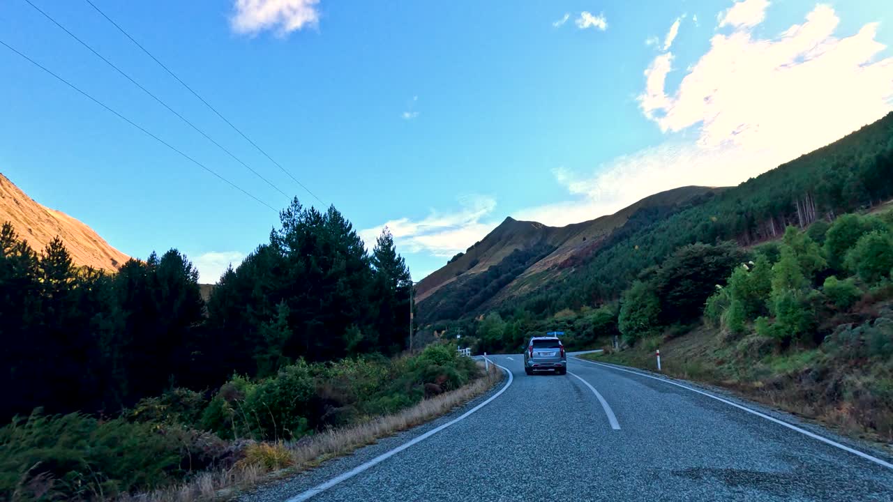 Vehicle travels on winding mountain road, surrounded by trees, under clear daylight, wide angle view