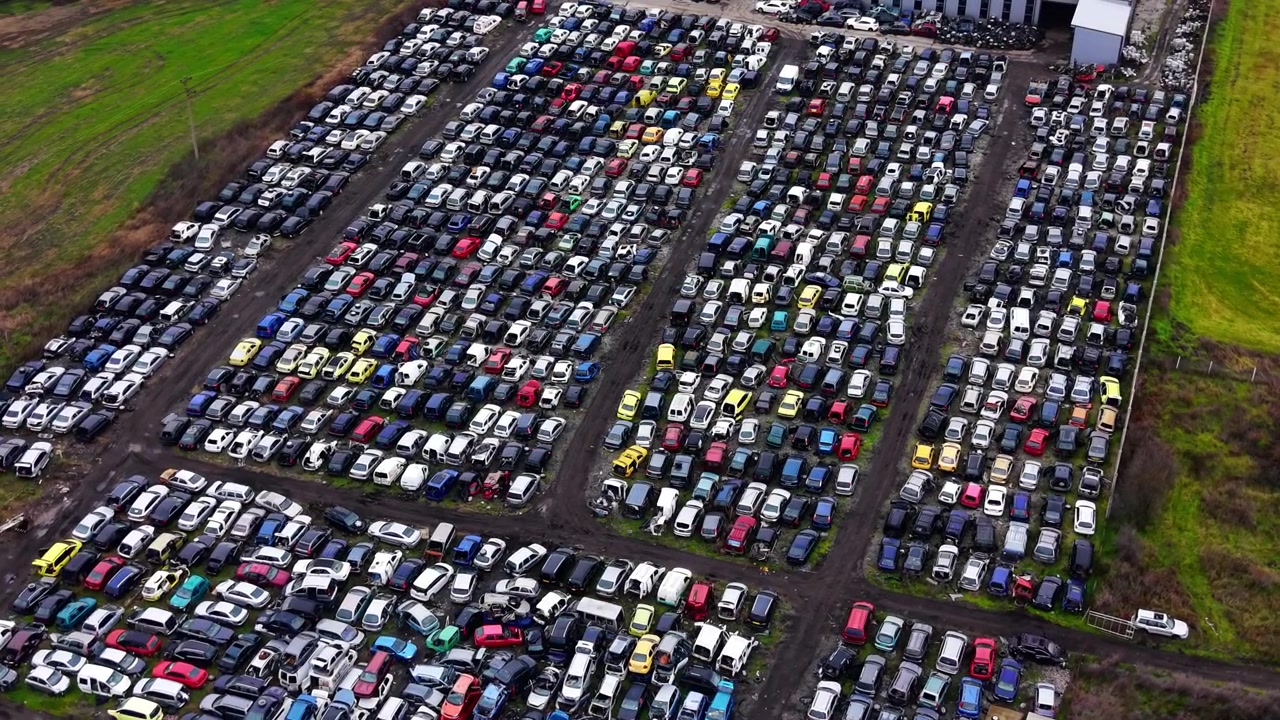 Ampia vista aerea di un grande sfasciacarrozze, Bulgaria. Prospettiva drone elevata su centinaia di auto rottamate colorate in più file con campi verdi su tutti i lati.