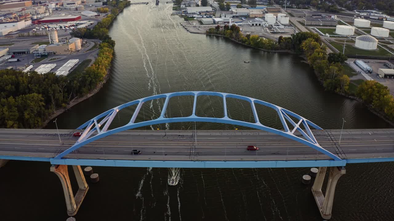 The Leo Frigo Memorial Bridge stretches across the Fox River toward downtown Green Bay, where golden sunset light reflects on the water and illuminates the industrial landscape beyond