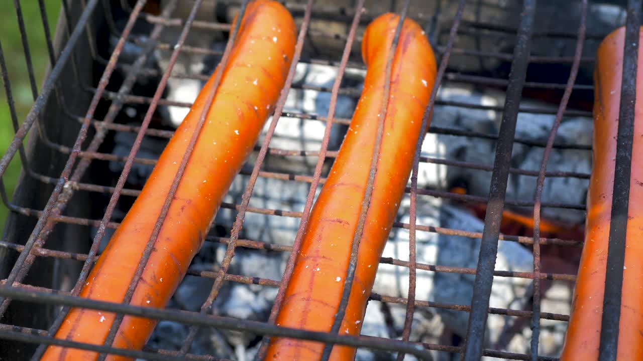 Cottura di salsicce di carne su un vecchio barbecue arrugginito all'aperto, primo piano
