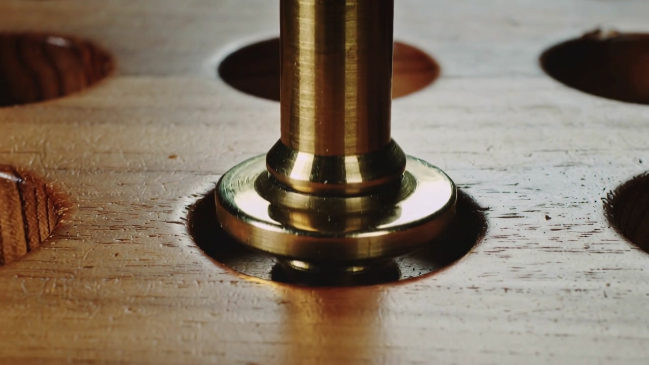 After mechanism release, lifting brass peg rising from countersunk wooden board for inspection