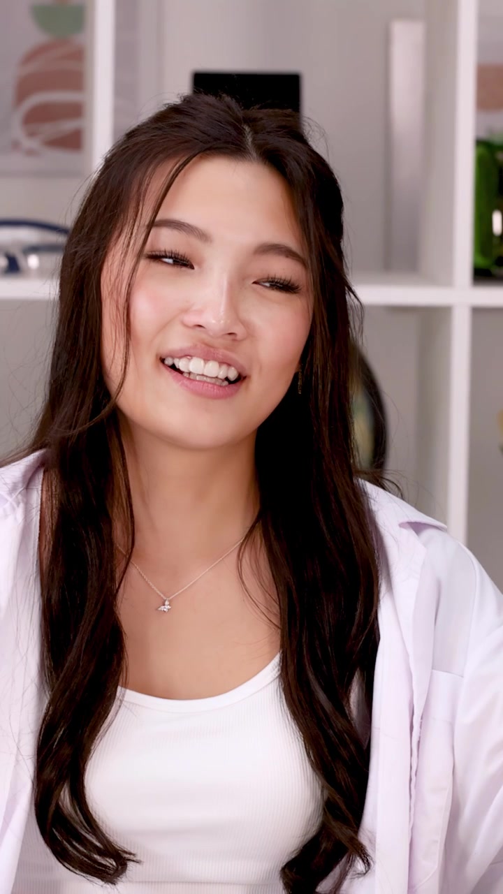 Asian student in white lab coat explains a concept using hand gestures in science classroom.