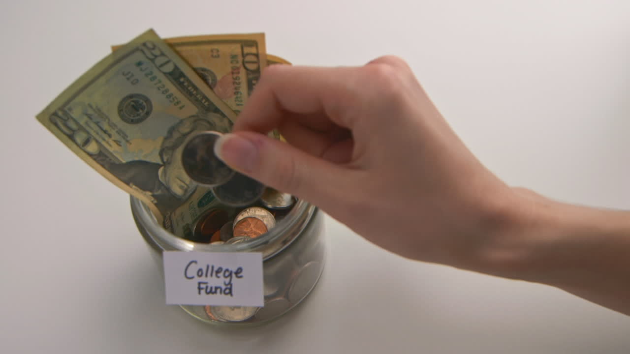 A caucasian woman's hand puts two American quarters into a "College Fund" jar